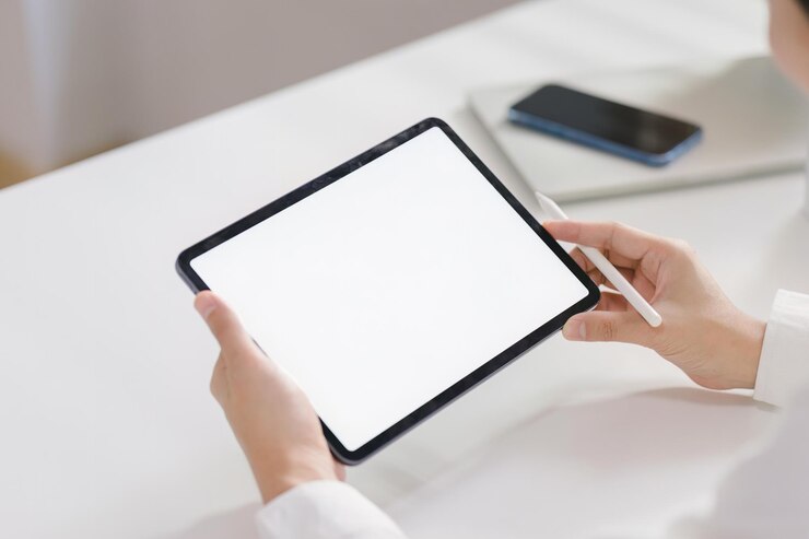 Photo 後ろから見ると,ビジネスマンが自宅のオフィスの机に座って,ホワイトスクリーンデジタルタブレットコンピュータを保持し,使用しているのが見えます.