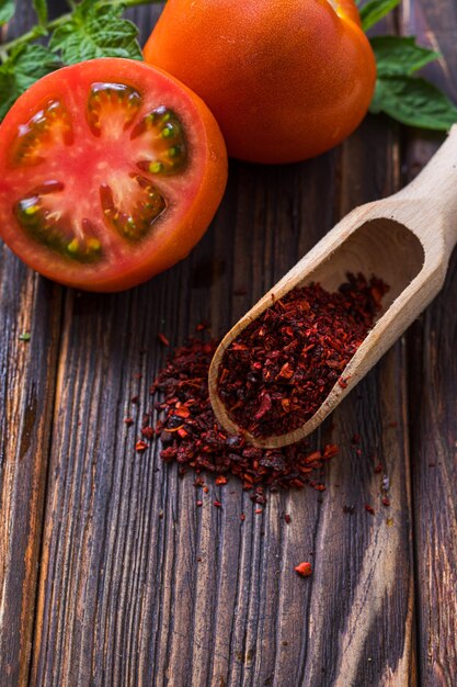 From above ripe fresh tomatoes and wooden scoop filled with dry tomato seasoning placed on wooden surface Organic ingredients for cooking at home