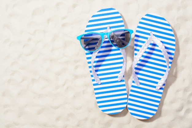 From above shot of striped flip flops on sand with sunglasses