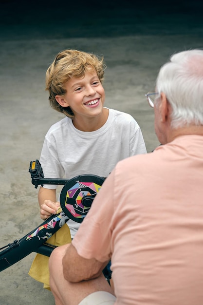 Сверху улыбающийся внук сидит с велосипедом и с любовью смотрит на дедушку урожая
