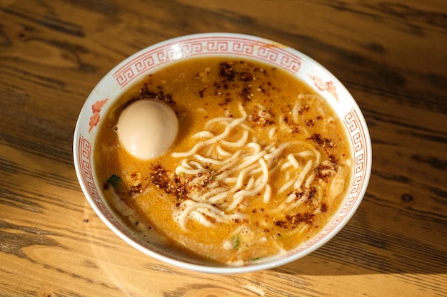 テーブルの上の白いボウルにゆで卵と麺が入ったおいしいラーメンスープの上から