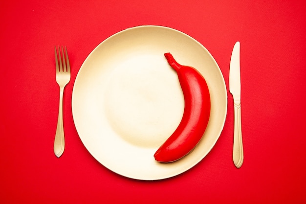 From above of tasty raw whole red banana served on white plate with fork and knife