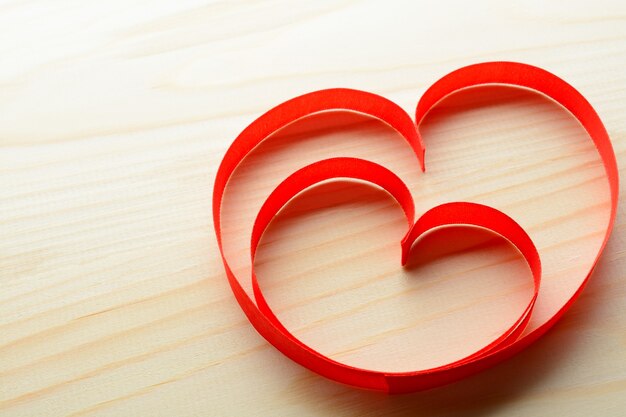 From above two red ribbons in heart shape on wooden background.