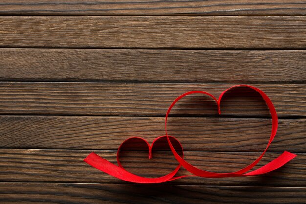 From above two red ribbons in heart shape on wooden background.