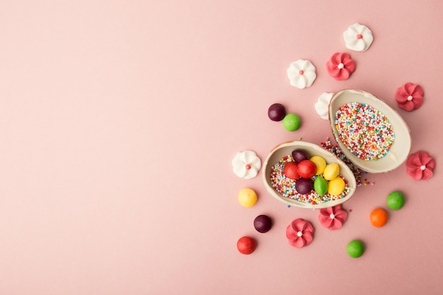 From above view of chocolate egg halves filled with sprinkles and candies arranged on pink