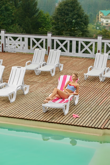 From above view of girl, relaxing on deck-chair near pool.