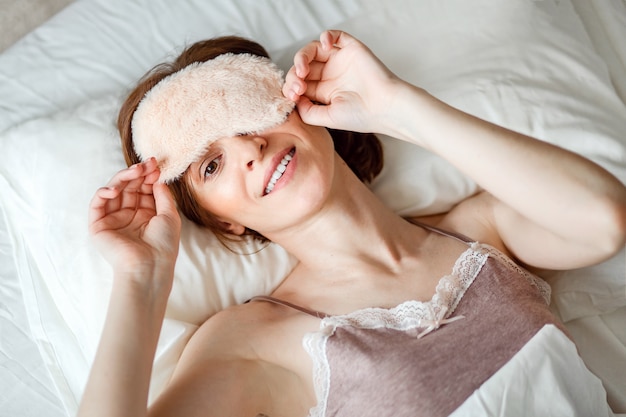 From above, a view of a healthy young woman laughing, removing her sleeping mask after a good night's rest is filmed.