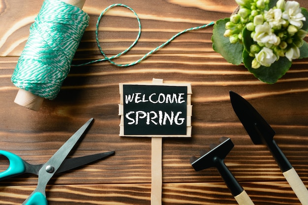 From above Welcome Spring sign and tools for gardening on wooden table