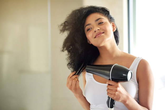 濡れたものから完全で素晴らしいものまで自宅でヘアドライヤーで髪を乾かす魅力的な若い女性のショット