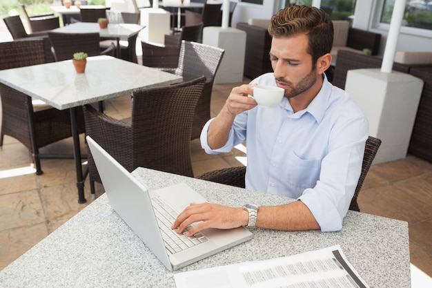 Fronsende jonge zakenman die bij laptop het drinken koffie werkt