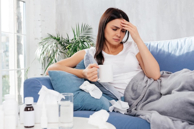 Fronsende vrouw die naar beneden kijkt en vingers op het voorhoofd houdt met een kop warme drank in de hand