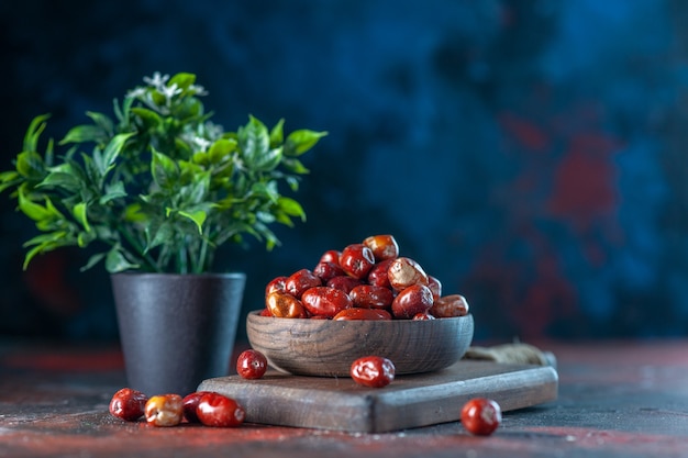 Vista frontale ravvicinata di frutti freschi di silverberry crudi in una ciotola su un tagliere di legno e un vaso di fiori su uno sfondo di colori misti