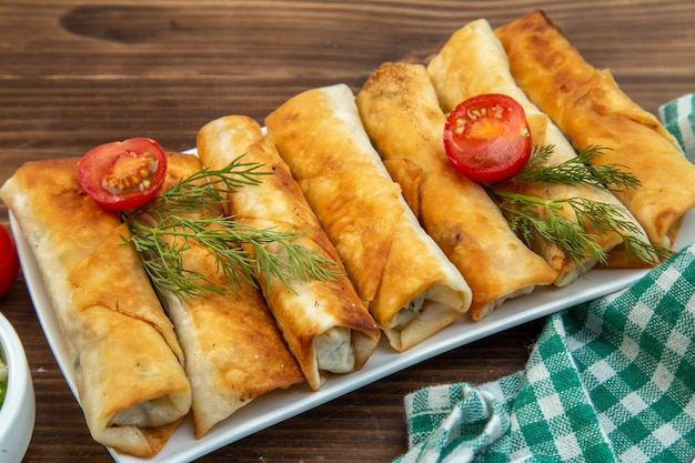 front close view fried greens pastries with red tomatoes on brown surface