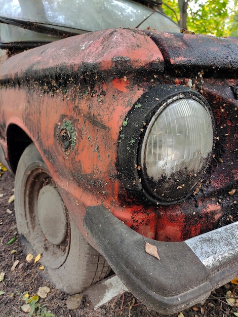 The front of a dirty old rusty car covered in rust You can see the headlight and the wheel