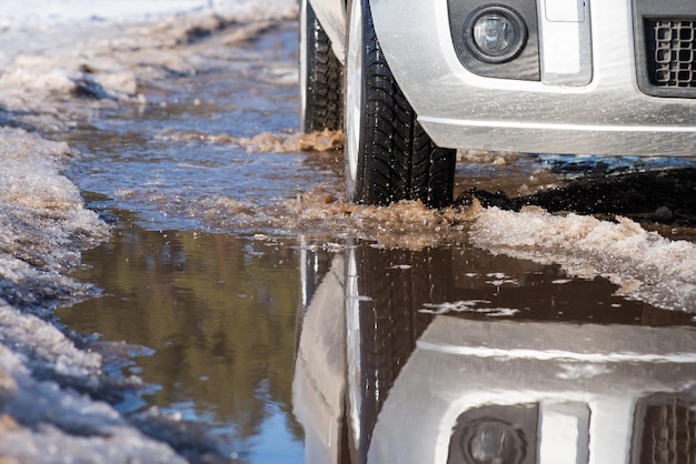 Front part of car on the muddy road with ponds spring thaw mash\
of snow and water on the tracks