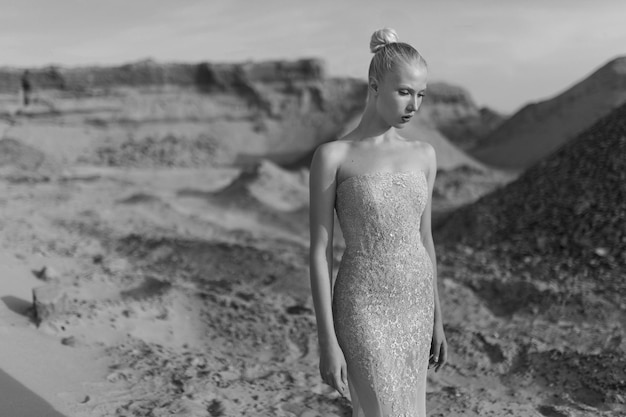 Front portrait of a beautiful young woman dressed in a gorgeous gilded fitted dress, posing in the desert at sunset.