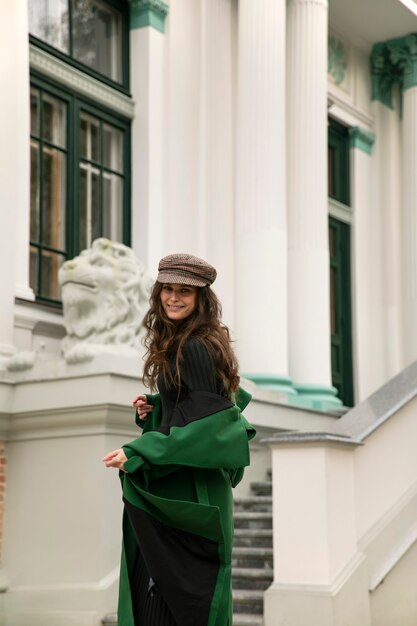 Front portrait of cheerful elegant young woman in hat and green coat smiling