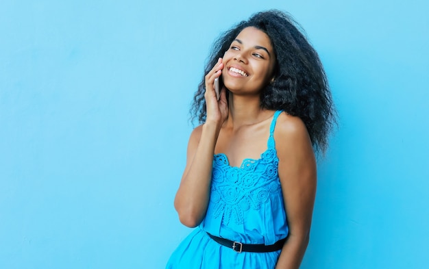 Front portrait of a joyful African American girl with shoulder-length messy black hair, who is laughing sincerely while talking on the phone and looking to the left