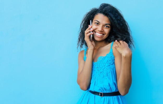 Front portrait of a joyful African American girl with shoulder-length messy black hair, who is laughing sincerely while talking on the phone and looking to the left