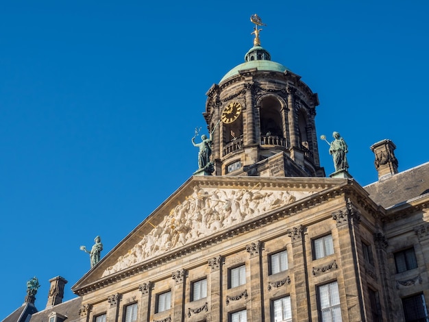 Photo the front of royal palace at the dam square, amsterdam, built as city hall during the dutch golden age in the seventeenth century, under blue sky