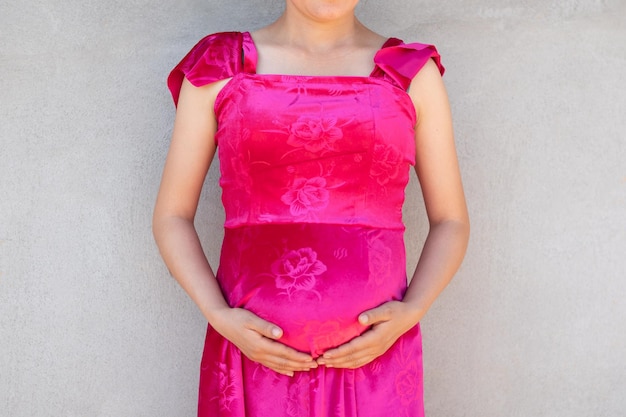 妊娠中の女性のフロント ショットは、胃の前部セメント壁の背景に触れています。