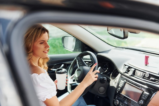 In front of steering wheel Young woman in casual clothes is sitting in her car at daytime