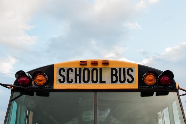 Front top view of a yellow school bus on a sky with clouds