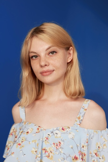 Front view of an adorable blonde young woman with blonde hair looking at camera isolated blue background