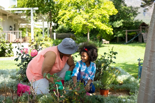 Front view of an African American grandmother with her granddaughter in the garden, kneeling, talking and gardening together. Family enjoying time at home, lifestyle concept