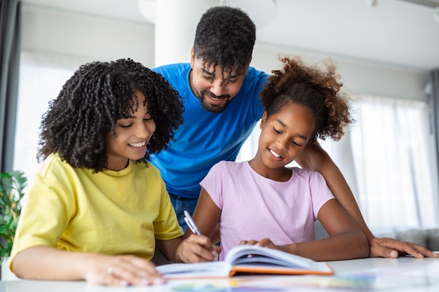 テーブルで娘の宿題を手伝っているアフリカ系アメリカ人の両親の正面図 両親によってホームスクーリングされている若い女の子の写真