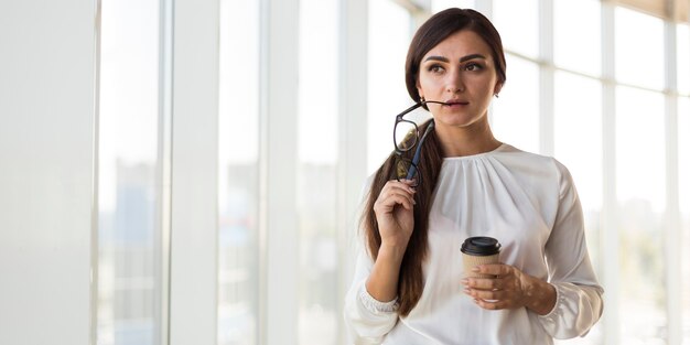 Front view of alluring businesswoman posing with glasses and coffee