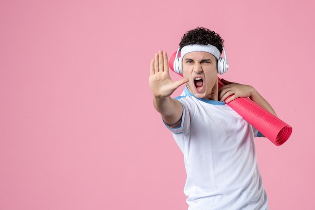 Front view angry young male in sport clothes with yoga mat