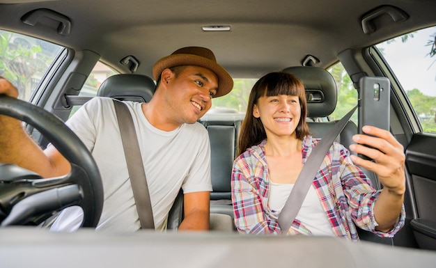 写真 車に座ってスマートフォンを見ている正面図アジアのカップルの幸せ旅行の概念安全第一保険の概念