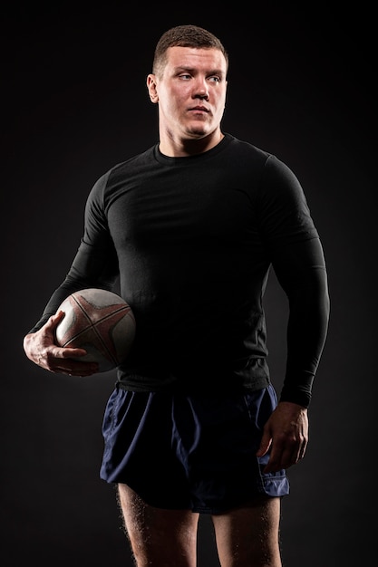 Front view of athletic male rugby player posing while holding ball