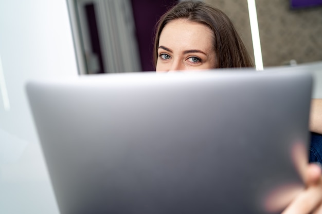 Foto vista frontale della ragazza caucasica attraente che per mezzo del computer portatile. computer portatile sulla vista frontale con la donna sullo sfondo.