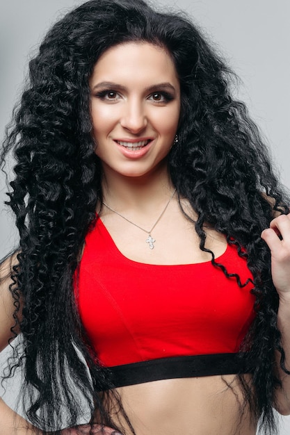 Front view of attractive long curly haired girl in sports red top smiling at camera Sexy and hot dancing woman with perfect body sedactive posing Concept of sport dance helthy lifestyle