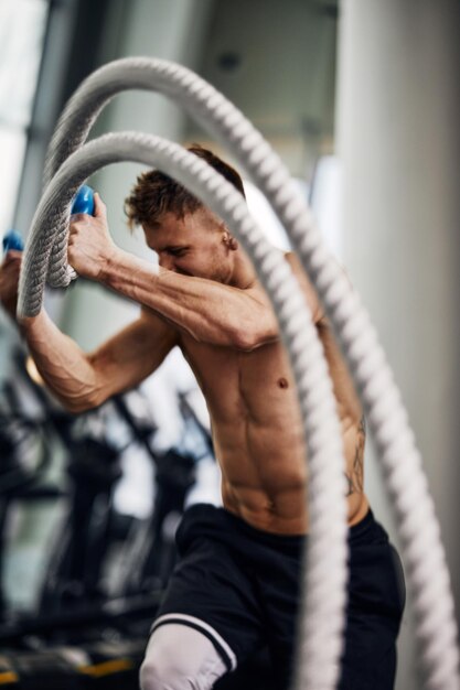 Front view of attractive young fit and toned sportswoman\
working out with battle ropes motion blur