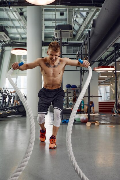 Front view of Attractive young fit and toned sportswoman working out with battle ropes Motion blur