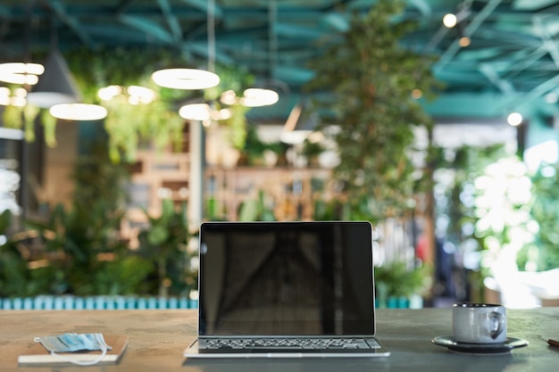 Photo front view background image of opened laptop with blank screen in modern eco-friendly cafe interior decorated with fresh green plants, copy space
