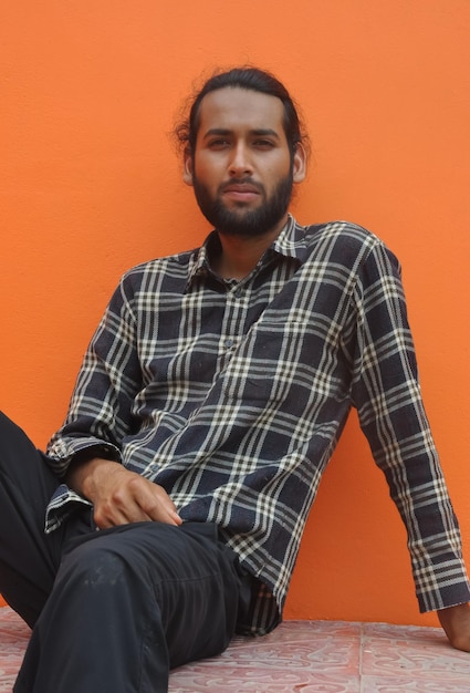 Front view of a bearded young man looking at camera sitting against orange wall with copy space
