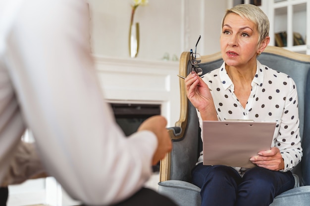 Photo front view of a beautiful professional senior caucasian female psychoanalyst explaining something to her client