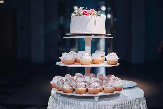 테이블에 꽃과 함께 아름 다운 웨딩 케이크의 전면 보기. 축하를 위한 맛있는 디저트. 배경에서 사랑스러운 쌍입니다. 사랑, 제과, 비스킷의 개념.