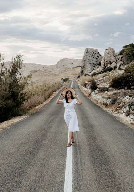 Foto vista anteriore di una bella giovane donna in abito bianco in piedi sulla strada aperta