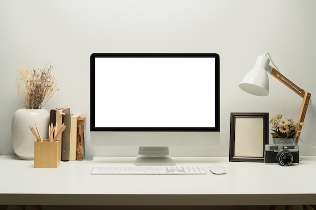 Front view of blank screen computer with keyboard lamp picture frame and books on white table