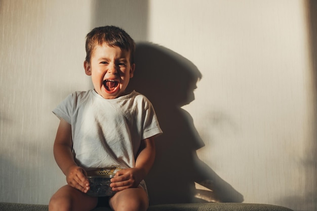 Front view of a boy sitting on sofa at home eating blueberry facial expressions