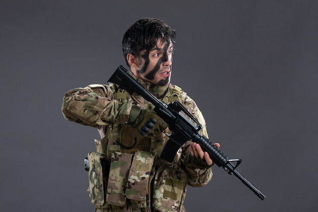 Вид спереди храброго солдата, сражающегося в камуфляже с пулеметом на темной стене