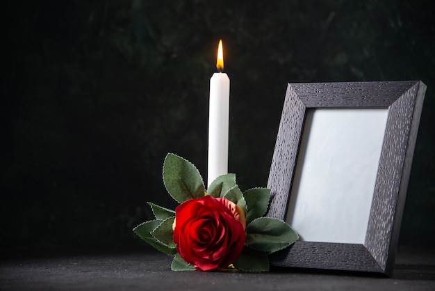 Front view of burning candle with picture frame on dark surface