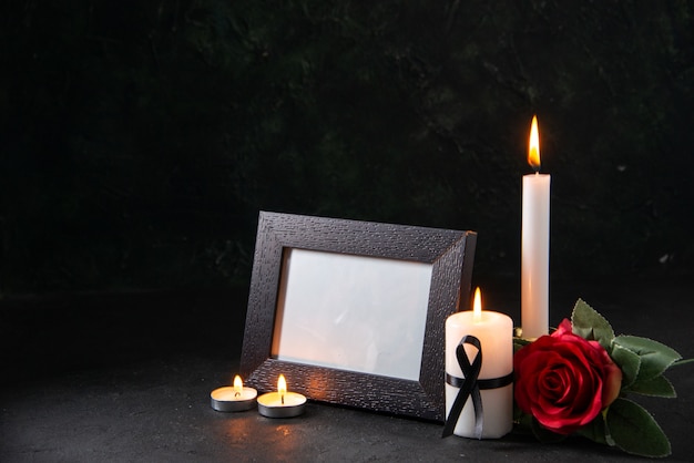 Front view of burning candles with picture frame on dark surface