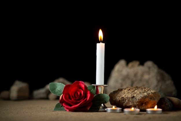 Front view of burning candles with red flower dark surface