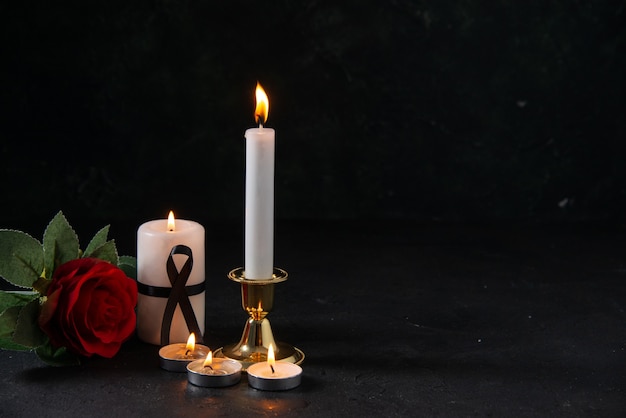 Front view of burning candles with red flower on a dark surface